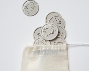May include: A small white drawstring bag with the text "MC SILVER LININGS" printed on the front. The bag is filled with gray wax seals with a floral design.