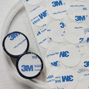 May include: A close-up of a pile of white adhesive tape circles with the 3M logo and the text "9448A Double Coated Tissue Tape" printed on them.