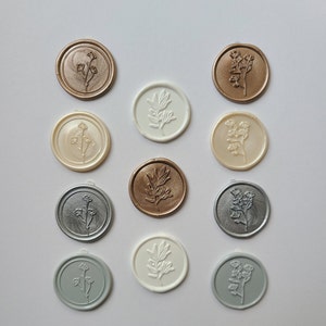 May include: Twelve wax seals with different floral designs. The seals are in various colors, including gold, silver, white, and gray.