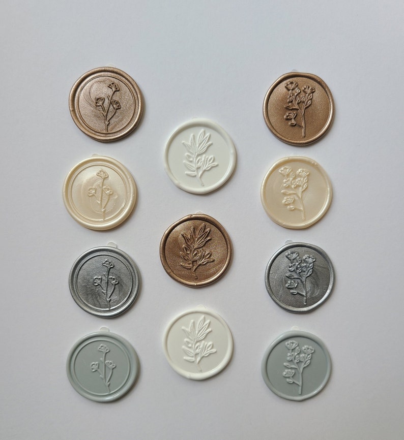 May include: Twelve wax seals with different floral designs. The seals are in various colors, including gold, silver, white, and gray.