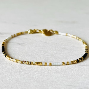 Peut inclure: Un bracelet délicat en or avec des perles noires, blanches et dorées. Le bracelet est composé de petites perles uniformément espacées.