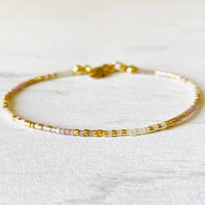 Peut inclure: Un bracelet délicat en or avec des perles blanches et roses. Le bracelet est composé de petites perles uniformément espacées.