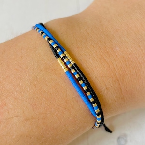 Peut inclure: Un bracelet superposé avec des perles bleues, noires et dorées. Le bracelet est attaché avec un cordon noir.