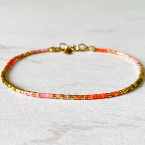 Peut inclure: Un bracelet délicat en chaîne dorée avec des perles roses et orange. Le bracelet est composé de petites perles espacées uniformément.