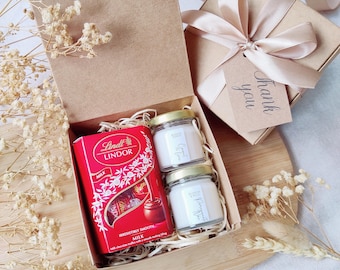 May include: A gift box with a red Lindor chocolate box, two small glass jars of candles, and a gift box tied with a ribbon. The candles are labeled "Cinnamon Spice" and "Pomegranate Spice". The gift box has a "Thank you" tag.
