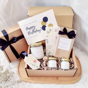 May include: A gift box containing a birthday card, candles, and a bar of soap. The card says "Happy Birthday!" with a message from "Anita." The box is tied with a black ribbon. The soap bar is wrapped in brown paper and tied with a black ribbon.