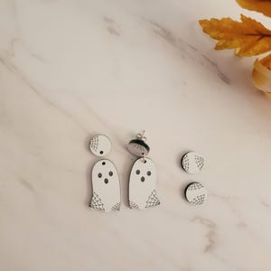 Puede incluir: Pendientes blancos con forma de fantasma con ojos de puntos negros y un diseño de telaraña. Los pendientes forman parte de un conjunto de joyas con temática de Halloween, que incluye dos pares de pendientes de botón con un diseño de telaraña.