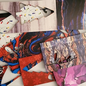 May include: A collection of decorative boxes with various patterns and cutouts. Designs include a Christmas tree shape, plaid, houndstooth, and abstract art. Colors range from red and black to blue and purple.