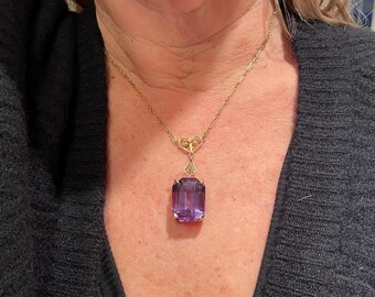 Puede incluir: Un collar de cadena de oro con un delicado colgante que presenta una gran piedra preciosa púrpura facetada.