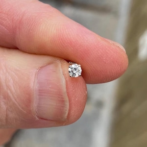 Könnte beinhalten: Ein einzelner Diamant-Ohrstecker mit einem runden Stein, der in einer silbernen Fassung gefasst ist.