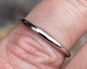 May include: A thin, polished silver-colored metal ring with a smooth, rounded band. The ring features a simple, minimalist design with a reflective surface that catches the light, showcasing a clean and uniform circular shape throughout the band.
