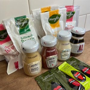 May include: An assortment of condiments and dressings, including Heinz Dijon mustard, ketchup, and mayonnaise, alongside Marzetti dressings and Paladin olive oil packets. The products are in various containers, including glass jars and plastic packets.