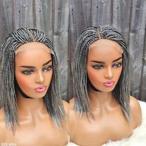 May include: Two wigs on display. Each wig features a braided style with a mix of black and grey strands. The wigs are styled with a centre part and fall to the shoulders. The wigs are displayed on mannequin heads.