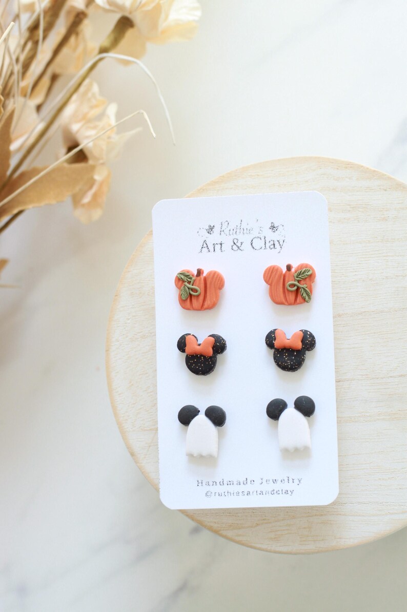 Peut inclure: Carte de bijoux faits &agrave; la main avec trois paires de boucles d'oreilles sur le th&egrave;me d'Halloween. Les boucles d'oreilles comprennent des citrouilles oranges avec des feuilles vertes, des t&ecirc;tes de Minnie Mouse noires et scintillantes avec des n&oelig;uds orange et des fant&ocirc;mes blancs.