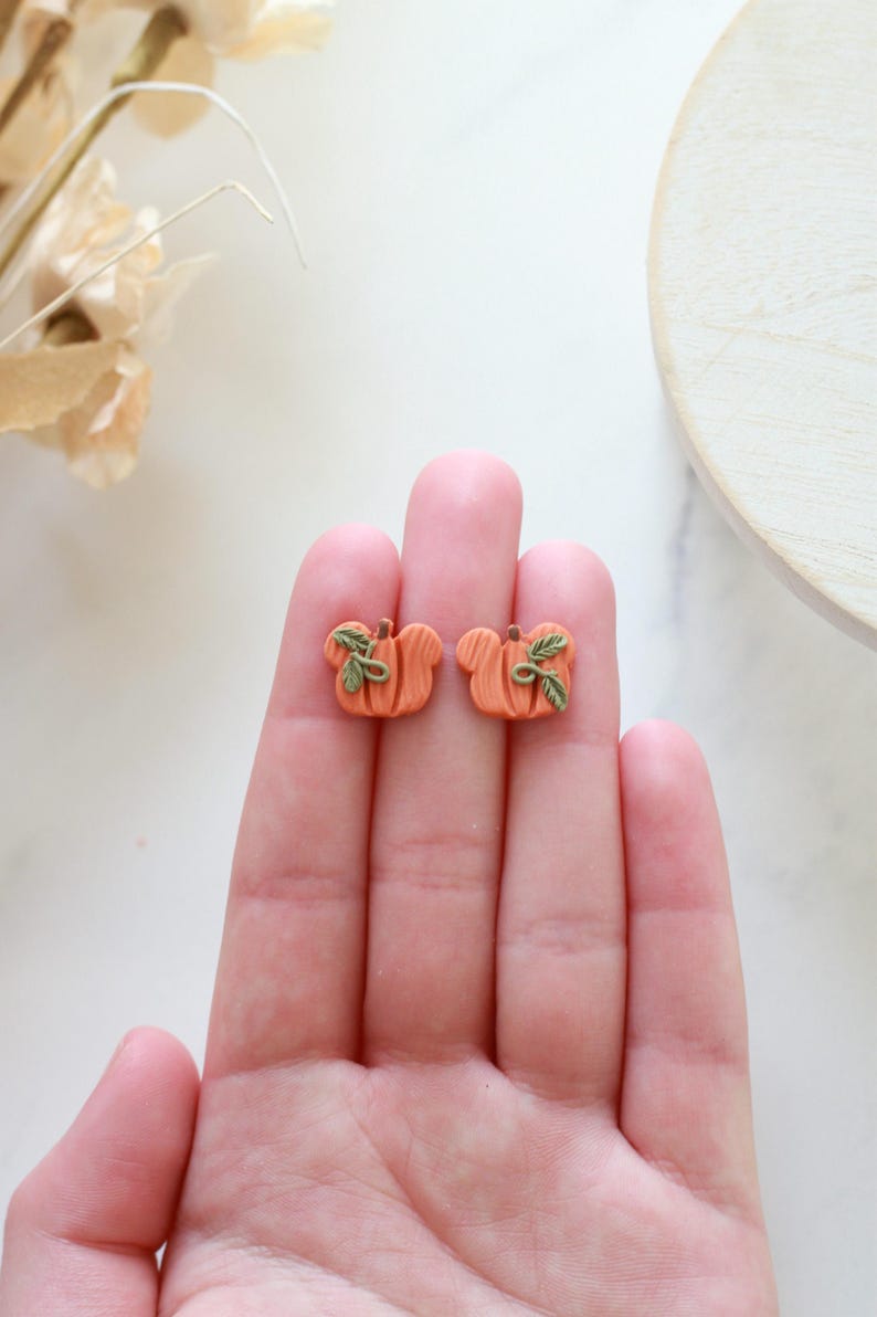 Peut inclure: Deux boucles d'oreilles clous en forme de citrouille orange avec des d&eacute;tails de feuilles vertes. Ces boucles d'oreilles sur le th&egrave;me de l'automne sont un accessoire charmant. Chaque boucle d'oreille mesure environ 1 cm.