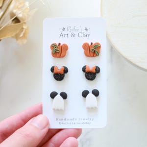 Peut inclure: Une carte pr&eacute;sentant six paires de boucles d'oreilles en argile faites &agrave; la main. Les boucles d'oreilles comprennent des citrouilles oranges avec des feuilles vertes, des t&ecirc;tes de Minnie Mouse noires avec des n&oelig;uds orange et des formes de fant&ocirc;mes blancs avec des t&ecirc;tes noires.