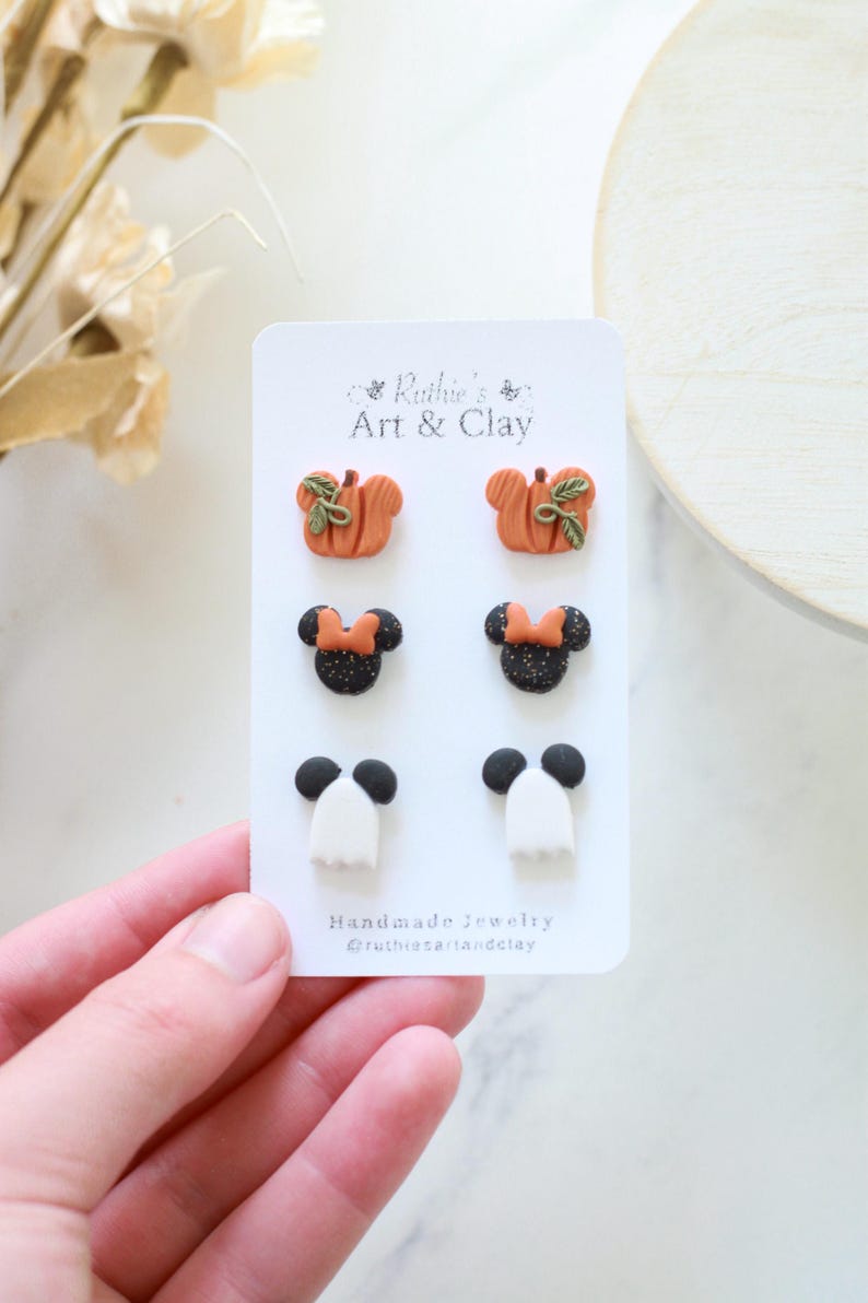 Peut inclure: Une carte pr&eacute;sentant six paires de boucles d'oreilles en argile faites &agrave; la main. Les boucles d'oreilles comprennent des citrouilles oranges avec des feuilles vertes, des t&ecirc;tes de Minnie Mouse noires avec des n&oelig;uds orange et des formes de fant&ocirc;mes blancs avec des t&ecirc;tes noires.