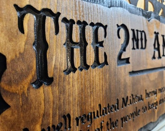 May include: A wooden sign with black lettering that reads "THE 2ND AMENDMENT well regulated Militia, being necessary to the security of a free State, the right of the people to keep and bear Arms, shall not be infringed."