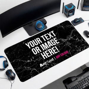 May include: A rectangular black mouse pad with a white marble-like pattern. The text "YOUR TEXT OR IMAGE HERE!" is prominently displayed in white, with "Any Font | ANY COLOUR" below it. The pad is on a white desk with computer peripherals.
