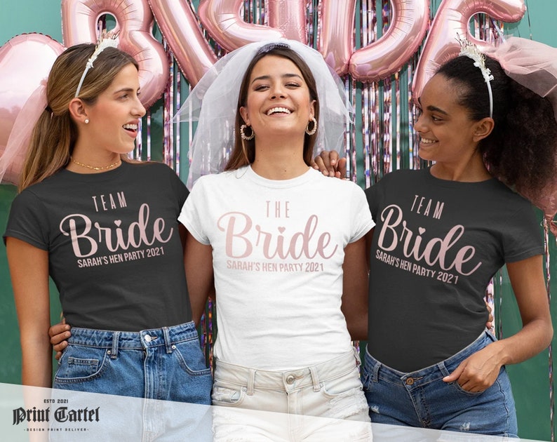 K&ouml;nnte beinhalten: Drei schwarze und wei&szlig;e T-Shirts mit dem Text "Team Bride" und "The Bride" in rosa Schrift. Die Shirts sind f&uuml;r eine Junggesellinnenparty und haben das Jahr 2021 aufgedruckt.