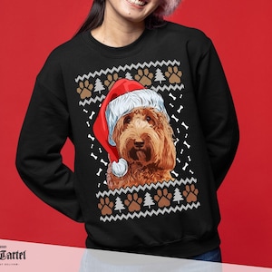 Puede incluir: Sudadera negra con un perro marrón con un gorro de Papá Noel. El diseño incluye huellas de patas, árboles de Navidad y patrones de huesos. La sudadera tiene cuello redondo y mangas largas, ideal para la temporada navideña.