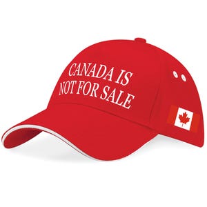 May include: A red baseball cap with the text "CANADA IS NOT FOR SALE" in white. The cap has a white trim on the peak and a small Canadian flag on the side.