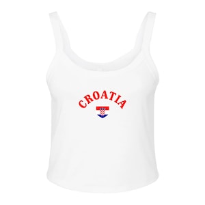 May include: White tank top with the word "Croatia" in red arched across the chest. Below the text is a small emblem of the Croatian flag. The tank top has a scoop neck and wide straps.