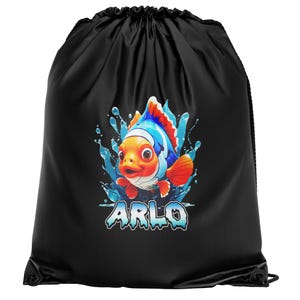 Puede incluir: Bolsa con cordón negra con un dibujo de pez de dibujos animados naranja, azul y rojo, rodeado de salpicaduras de agua. El nombre "ARLO" está escrito en azul y blanco. La bolsa es de tela negra.