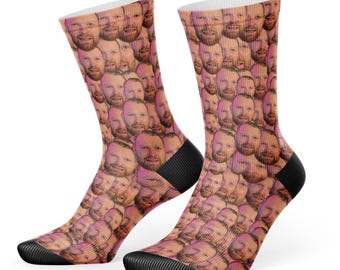 Peut inclure: Une paire de chaussettes blanches avec un motif répété d'un visage d'homme. Les chaussettes sont noires au niveau des orteils et des talons.