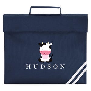 May include: A navy blue school bag featuring a cartoon cow design and the name "HUDSON" in white. The bag has a handle and white stripes. A practical and charming school accessory.