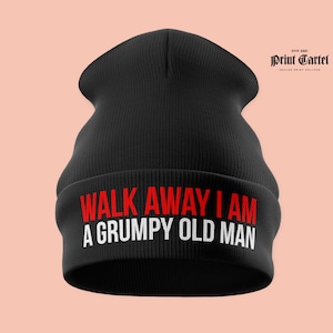 以下が含まれることがあります： 赤と白で「WALK AWAY I AM A GRUMPY OLD MAN」の文字が入った黒いニット帽。折り返しのあるつばと、柔らかく質感のある外観です。プリントカルテルのロゴが右上隅にあります。