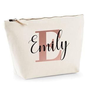 Puede incluir: Una bolsa de lona blanca con cremallera con una "E" de oro rosa y el nombre "Emily" impreso en negro.