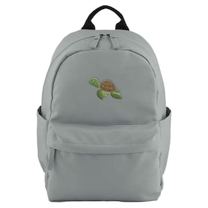May include: A gray backpack with a black handle and zipper pulls. The front of the backpack features a green and brown embroidered sea turtle. The backpack has two side pockets and a front pocket.