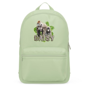 May include: A light green backpack featuring a graphic of two gorillas and tropical leaves. The name "DAISY" is printed in a decorative font below the gorillas. The backpack has a front zippered pocket and a top handle.
