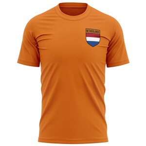 Pode incluir: Camiseta laranja com um pequeno patch bordado com a bandeira holandesa e a palavra "Pa&iacute;ses Baixos" nele.