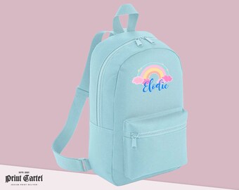 May include: A light blue backpack with a rainbow and cloud design and the name "Elodie" embroidered on the front.