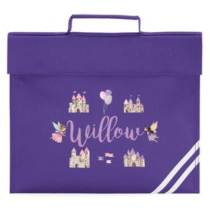 May include: Purple school satchel with a handle and a flap closure. The satchel features a fairy and castle design with the name "Willow" in cursive. White stripes run along the lower right corner.