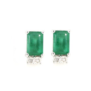 Puede incluir: Un par de pendientes de botón de esmeralda y diamantes con corte esmeralda. Las esmeraldas de color verde brillante están engastadas en un metal plateado con un grupo de pequeños diamantes debajo de cada esmeralda.