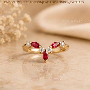 Peut inclure: Une bague en or en forme de V ornée de trois rubis rouges taille marquise et de quatre diamants blancs taille ronde disposés symétriquement. Le texte LONDONJEWELLERS est visible en haut. La bague possède un anneau en métal poli.
