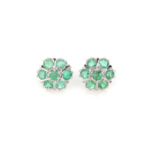 May include: A pair of stud earrings featuring a floral design. Each earring has a cluster of round, vibrant green gemstones set in a silver-colored metal. The gemstones are arranged to resemble flower petals.