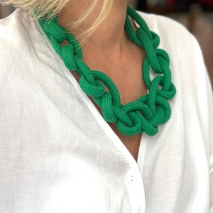 Puede incluir: Un conjunto de collar y pulsera de cuerda verde. El collar es grueso y grueso, con un diseño anudado. La pulsera es una versión más pequeña del collar, con el mismo diseño anudado.