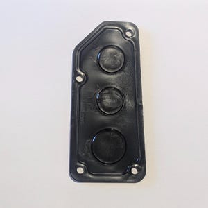 May include: A black plastic component, rectangular with rounded corners, featuring three raised circular areas. It has several small holes and the text "8008" and "TOP".