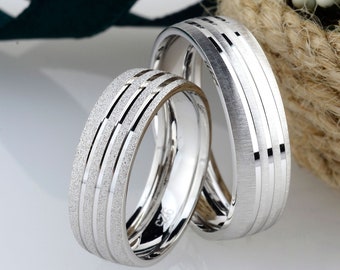 May include: Two silver wedding bands with a textured finish. The bands are stacked on top of each other.