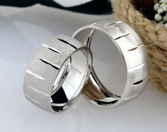 May include: Two silver wedding bands with a textured design. The bands are stacked on top of each other.