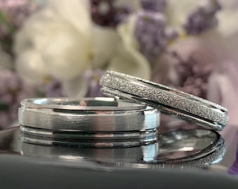 May include: Two silver wedding bands. One band has a smooth finish, while the other has a textured, brushed finish.