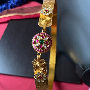 May include: A gold waist belt with three decorative round ornaments. The ornaments are adorned with pink and white stones.