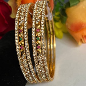 May include: A set of four gold bangles with a row of clear stones and small red and green stones.