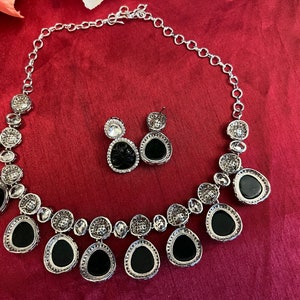 Pu&ograve; includere: Una collana d'argento con un designo in cristallo nero e trasparente. La collana ha uno stile a catena e presenta un ciondolo con pi&ugrave; cristalli neri e trasparenti. La collana &egrave; accompagnata da un paio di orecchini abbinati con cristalli neri e trasparenti.