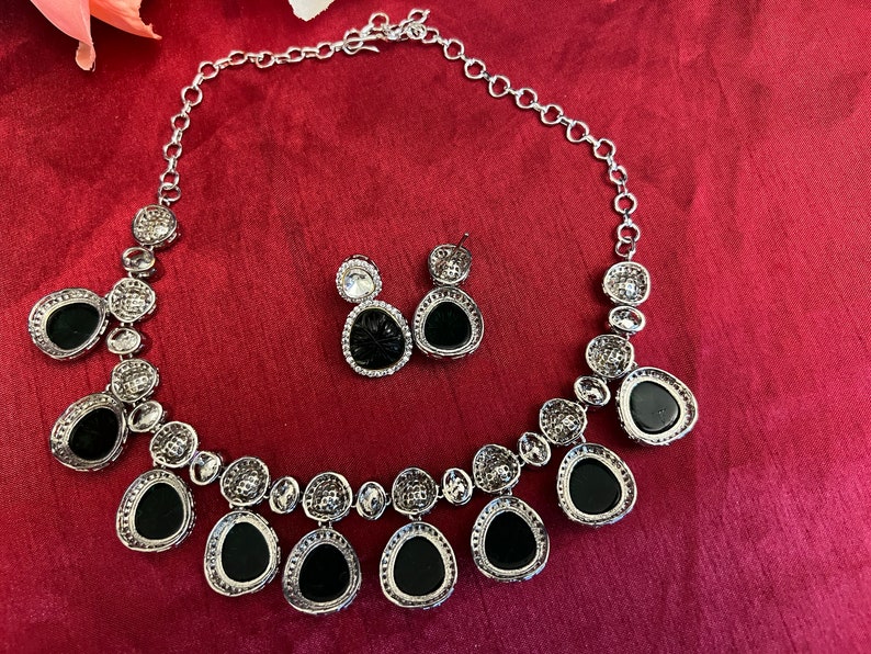 Pu&ograve; includere: Una collana d'argento con un designo in cristallo nero e trasparente. La collana ha uno stile a catena e presenta un ciondolo con pi&ugrave; cristalli neri e trasparenti. La collana &egrave; accompagnata da un paio di orecchini abbinati con cristalli neri e trasparenti.