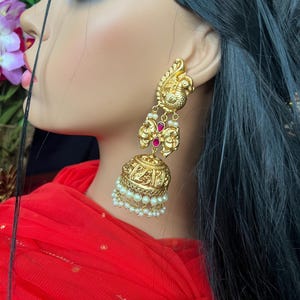 May include: Gold earrings with a peacock design, red stones, and pearl accents.